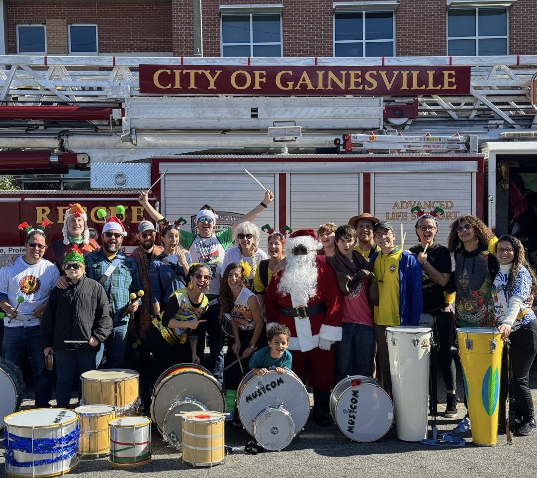 Bloco GNV members in matching black shirts with drums, posing in front of a City of Gainesville fire truck during the holiday parade