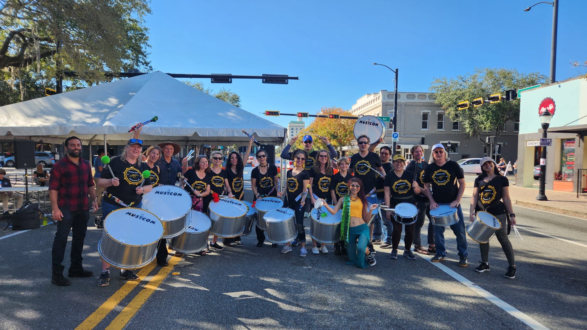 Bloco GNV members holding drums and mallets while posing for a group photo on a street in downtown Gainesville